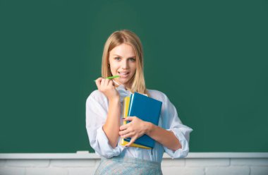 Sınıfta okuyan genç bir üniversite öğrencisinin portresi. Tahta altyapısı var. Kalem ve kitapla gülümseyen yaratıcı genç bayan öğrenci.