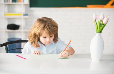 Okuldaki çocuklar, sınıftaki çocuklar. Kitapla yazı yazan ve sınıftaki masada oturan okul çocuğu.