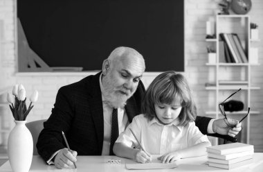 Yaşlı öğretmen ve genç okul çocuğu okulda ödev yapıyor. Öğretmenler Günü