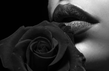 Dudakları rujla yakın plan. Kırmızı güllü bir kadın, makro, siyah arka planda. Güllü güzel kadın dudakları