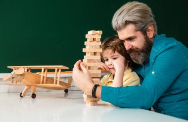 Baba ve oğul evde jenga oynuyorlar. İlkokul ve eğitim. Sevimli öğrenci ve babasının okul işleri.