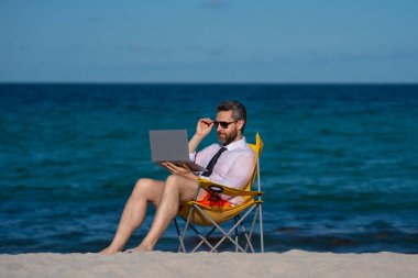 Deniz sahilinde dizüstü bilgisayar kullanan iş adamı. Yaz tatilindeki çılgın iş adamı. Heyecanlı iş adamı, çılgın komedi dünyası konsepti. Uzaktan kumanda çalışıyor. Yaz iş hayalleri