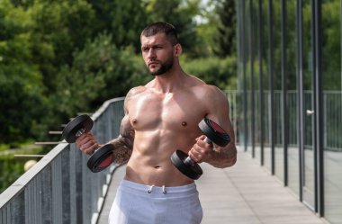 Halterle egzersiz yapan bir adam. Formda bir model ağırlık kaldırıyor, spor salonunda egzersiz yapıyor. Halterle antrenman. Güçlü, kaslı, formda, halterli ve ağır ağırlıklı bir adam. Kas pazıları için alıştırmalar