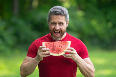 Karpuzlu adam suratı. Yazlık parkta karpuz yiyen komik, olgun bir adam. Yaz yemeği. Bahçede karpuz yiyen orta yaşlı bir adam. Adam dışarıda meyve yiyor. Karpuzun tadını çıkarıyorum.