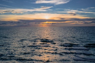 Gökyüzü ve bulutların arasından güneş batarken deniz batıyor. Okyanus ve gökyüzü arkaplanı, deniz manzarası.