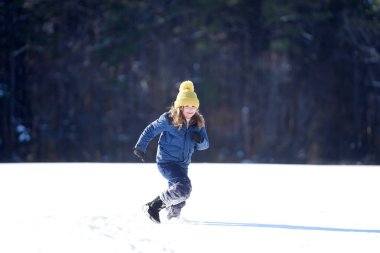 Çocuklar kış oyunu oynuyor. Çocuk kış şapkasıyla karda oynuyor. Sıcak giysili mutlu çocuk kar yağarken eğleniyor. İlk kar yağışında çocuk dışarıda karla oynuyor. Çocuklar için kış aktiviteleri