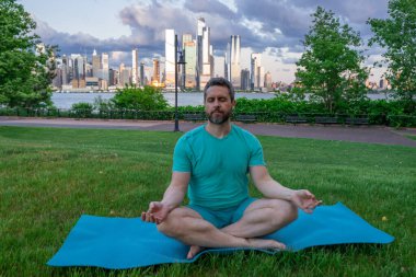 Hispanik Adam dışarıda otların içinde meditasyon yapıyor. Sporcu şehir parkında yoga yaparken asana meditasyonu yapıyor. Atletik erkek meditasyonu, rahatlama, sağlıklı yaşam tarzı kavramı. Açık havada meditasyon.