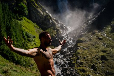 Yaz tatilindeki erkek turist. Yaz tatilinde çıplak gövdeli yakışıklı bir adam. Dışarıda seksi bir yürüyüşçü var. Şelale manzarasında yürüyen bir turist. İnsan Seyahati ve doğa