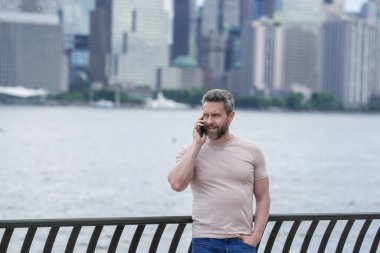 New York 'ta telefonla konuşan bir adam. İspanyol adam telefonda konuşuyordu. Tişörtlü adam cep telefonuyla konuşuyor. Cep telefonuyla konuşan adam. Şehirdeki turistin elinde akıllı telefon var