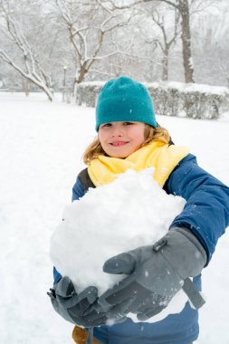 Soğuk bir kış gününde, kış parkında heyecanlı bir çocuk. Kışın karla oynayan sevimli bir çocuk. Kardan adamla komik çocuk portresi. Noel 'de kış aktiviteleri. Parkta kardan adam yapan çocuk