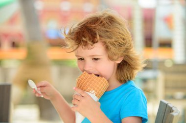 Güzel, gülümseyen beyaz bir çocuğun portresi lezzetli bir dondurma yiyor.