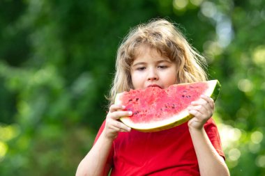 Kid 'in karpuzlu yaz portresi. Yazlık parkta karpuz yiyen komik çocuk. Bahçede karpuz yiyen bir çocuk. Çocuklar dışarıda meyve yer. Çocuk karpuz seviyor.