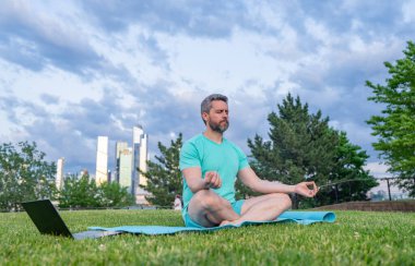 Latin Adam dışarıda otların içinde meditasyon yapıyor. Sporcu şehir parkında yoga yaparken asana meditasyonu yapıyor. Atletik erkek meditasyonu, rahatlama, sağlıklı yaşam tarzı kavramı. Açık havada meditasyon.