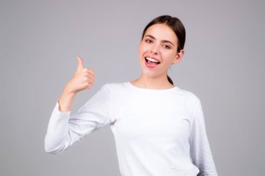 Gri arka planda izole edilmiş genç kız baş parmağını gösterdi. Kadın eli baş parmağını gösteriyor. Başparmak kaldıran bir el. Başparmağı havada Mutlu Kadın