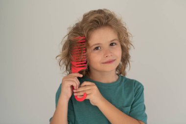 Oğlan saçını tarıyor. Kıvırcık saçlı çocuk saç fırçası ya da tarak tutuyor. Sağlıklı saçlar. Çocuk kontrolsüz saçlarını tarıyor.