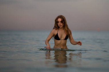 Yaz plajında bikinili genç bir kadın. Yazın denizde eğlenen seksi kadın. Seksi bikinili kadın, tropik bir plajda oynaşıyor. Yaz kızı deniz suyunda koşup sıçrıyor.