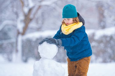Komik Çocuk kışın kardan adam için kartopu yapıyor. Çocuk karda oynuyor. Açık havada aktif kış oyunları. Çocuk karla oynarken eğleniyor. Çocuklar için açık havada kış tatili. Güneşli kış gününde çocuk oyunu