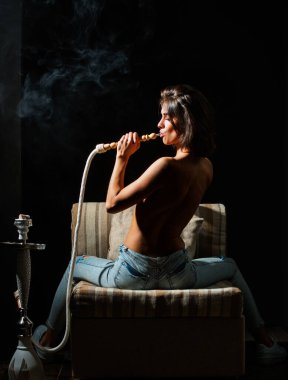 Siyahın üstünde nargile içen seksi çıplak kadın. Nargile gece hayatını tüttürür. Gece kulübü nargile salonu. Lüks bir gece kulübü. Nargile salonu atmosferi