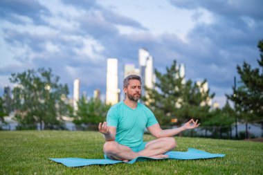 Nilüfer çiçeği içinde meditasyon yapan bir adam dışarıda çimlerde poz verir. Spor adamı, şehir parkında yoga yapıyor. Atletik erkek meditasyonu, rahatlama, aktif sağlıklı yaşam tarzı kavramı. Açık havada meditasyon.