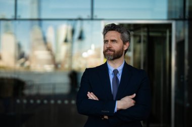Modern ofis binasının önünde duran kendine güvenen bir iş adamı. İş başarısı. Dışarıyı düşünen bir iş adamı. Takım elbiseli modern iş adamı ofis manzarasının yanında duruyor.