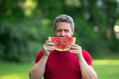 Karpuzlu adam suratı. Yazlık parkta karpuz yiyen komik, olgun bir adam. Yaz yemeği. Bahçede karpuz yiyen orta yaşlı bir adam. Adam dışarıda meyve yiyor. Karpuzun tadını çıkarıyorum.