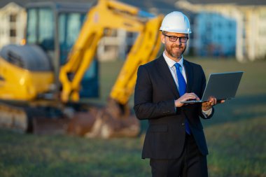 Başarılı bir inşaat işletmesi sahibi. Kazıcının yanındaki kask ve takım elbiseli inşaat işçisi. İnşaat alanının önünde kendine güvenen bir inşaat sahibi. İnşaat mühendisi.