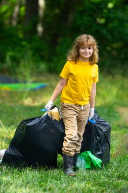 Çevre plastik kirliliği. Ormanda çöp toplayan ve elinde çöp torbası tutan gönüllü bir çocuk. Çevresel koruma. Çevre aktivisti. Çevre koruma ve atık kirliliği