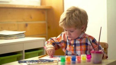 Anaokulu çocukları. Küçük şirin bir çocuk resmi ve çizimi. Pastel boyalı ve kağıda çizim yapan bir çocuk. Çocuklar için yaratıcı bir oyun. Suluboya kullanarak rengarenk boyalı bebek resmi.