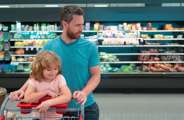 Baba ve oğul markette ürünlere bakıyor. Baba ve çocuk süpermarketten yiyecek alıyor.
