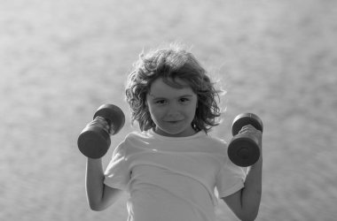 Kol kaslarını halterle şişiren sevimli çocuk. Dambılı spor çocukları.