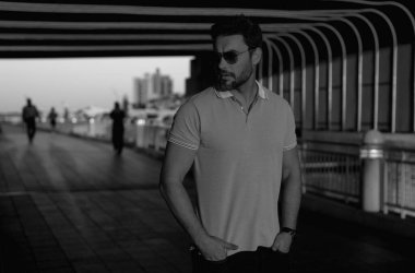 Şehir merkezinde sıradan, yakışıklı bir manken. İyi giyimli, gözlüklü ve polo pozu veren bir adam. Erkek model. Şehirde şık bir adamın portresi. Açık hava moda portresi