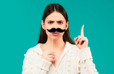 Takma bıyıklı kadın eğleniyor. Mavi arka planda parmakları yukarıda komik bir kadın oyuncu.