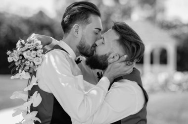 Evli LGBT çiftleri romantik bir düğün törenini bir buket çiçekle kutluyorlar. Düğünde eşcinsel öpücüğü. Evli eşcinsel çift öpüşüyor. Gey öpücüğünün yakın portresi