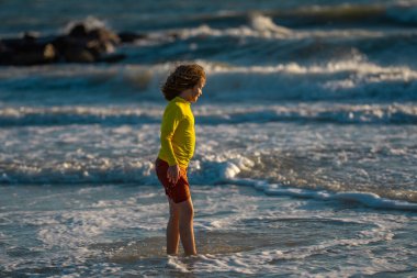 Çocuk tropikal deniz kıyısındaki tatil köyünde eğleniyor. Sörf kenarındaki su birikintisinin yanında koşan komik çocuk. Aktif çocuk yaşam tarzı, yaz tatilinde çocuklarla yüzme aktiviteleri.