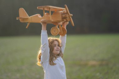 Çocuklar rüya görür. Mutlu çocuk dışarıda tahta uçakla oynuyor. Çocuk oyuncak uçakla oynuyor. Bir pilot olma hayali. Mutlu çocuk oyuncak uçakla oynuyor ve parkta rüya görüyor. Çocuk rüyaları. Çocuk