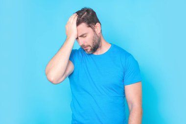 Migren ağrısı çeken bir adam. Sıkılmış adamın başı ağrıyor. Yorgun bir adam migrenle ya da baş ağrısıyla mücadele ediyor. Adamın başı ağrıyor, stüdyo mavisi arka planda izole edilmiş.