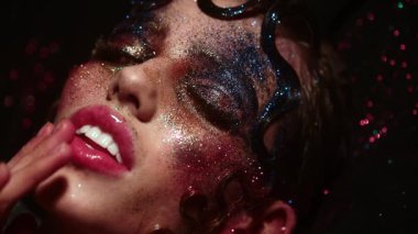 Güzellik suratında parıltı. Modellerin yüzüne parlak bir makyaj. Yaratıcı neon parıltılı yüz sanatı. Parıldayan kozmetik ürünleri olan seksi bir kadın. Renkli sim makyajı. Sinematik güzellik modeli metalik parlaklık. Sanat kadını yüzü