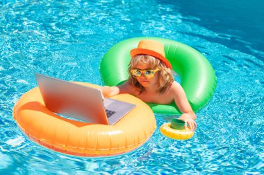 Çocuk dizüstü bilgisayarla havuzda dinleniyor. Çocuk internette dizüstü bilgisayarda çalışıyor, güneşli turkuaz bir su havuzunda yüzüyor. Dışarıda bilardoda dizüstü bilgisayarla çalış