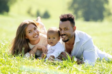 Çok ırklı ebeveynler ve parkta melez bir bebek. Dışarıda çok ırklı bir aile var. Bahçede melez bir bebek var. Çok ırklı bir aile. Çimlerde yatan çocuklu çok ırklı anne ve baba.