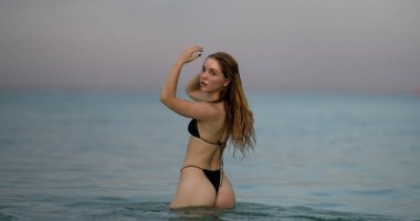 Sahilde şık bikinili güzel bir kadın. Sıcak yaz. Siyah bikinili mayolu, deniz suyunda rahatlayan mükemmel vücutlu güzel seksi kız. Suda poz veren güzel bir kadın.