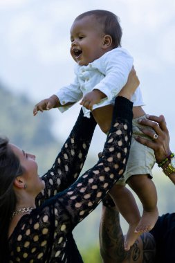Mutlu genç aile, farklı ebeveynler yaz bahçesinde bebekle eğleniyor. Dışarıda küçük bir çocuğu olan çok ırklı bir aile. Karışık ırk ailesi. Doğada çocuğu olan çok ırklı bir aile.