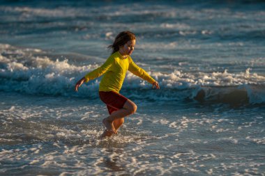 Çocuk yaz tatilinde sahilde koşuyor ve eğleniyor. Denizde oynayan mutlu çocuklar. Doğada denizli çocuklar. Deniz kıyısında tatilde deniz suyunda koşan mutlu çocuklar. Çocuk deniz sahilinde yürüyor.