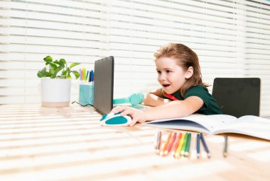 Akıllı okul çocuğu evde ödev yazıyor. Not defteri bilgisayarı olan küçük bir öğrenci çalışmaya hazır. Okul kumandası, online öğrenme. Evde öğrenim gören çocuk.
