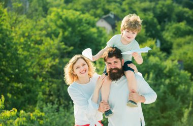Seyahat aile hayalleri. Baba, anne ve oğlu dışarıda oynuyorlar. Sevimli küçük çocuk kağıt uçak tutuyor. Baba oğlunu omuzlarında taşıyor.
