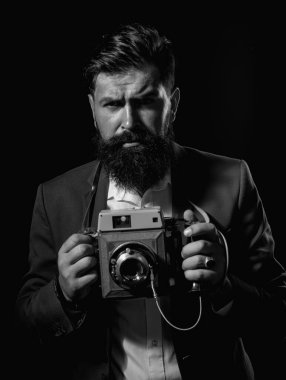 Fotoğraf makineli sakallı adam. Siyah arka planda izole edilmiş antika eski film kamerası olan ciddi bir erkek fotoğrafçının portresi.