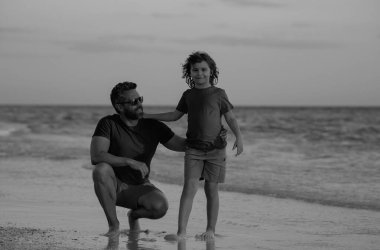 Baba ve oğul gün içinde plajda yürüyorlar. Arkadaş canlısı bir aile. Babalar Günü. Aşk ailesi, baba ve oğlu sahilde deniz doğasında birlikte yürürler. Ebeveynlik, babalık, babaların sevgisi.