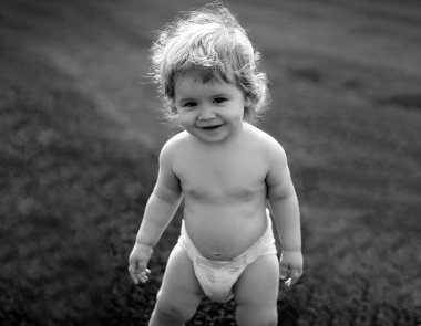 Yeşil çimlerin üzerinde, doğada oynayan, bez takmış küçük bir bebek. Çocuklar oynuyor. Bebek ve yaz güneşli hava. Küçük komik çocuk portresi. Sarışın çocuk, gülen duygu, gülen surat