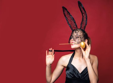 Paskalya bayramını kutlayan maskeli ve kulaklı seksi Paskalya tavşanı. Kırmızı arka planda izole edilmiş tavşan kostümlü tahrik edici genç bir kadın. Seksi tavşan konsepti
