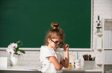 Kara tahtada gözlüklü inek öğrenci. Küçük tatlı liseli kız bir sınıfta ders çalışıyor.