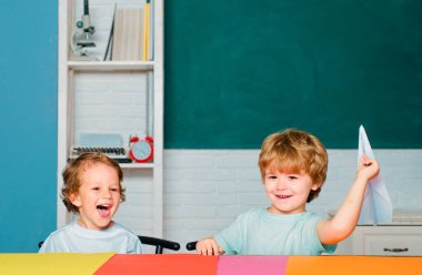 Sınıfta küçük şirin bir anaokulu çocuğu ders çalışıyor. Eğitimsel süreç. İlkokul ve eğitim. İlkokuldan komik çocuklar kağıt uçak tutup gülüyorlar.